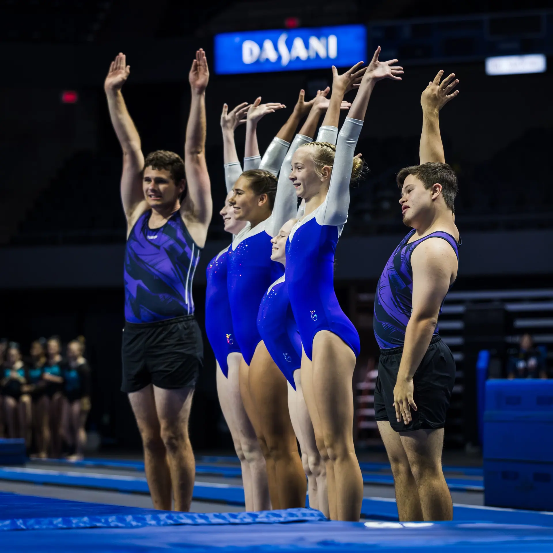 Four performers with hands raised, in blue