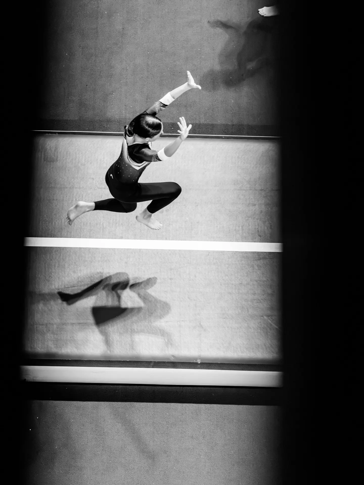 A gymnast in a full leap across a wide, empty floor