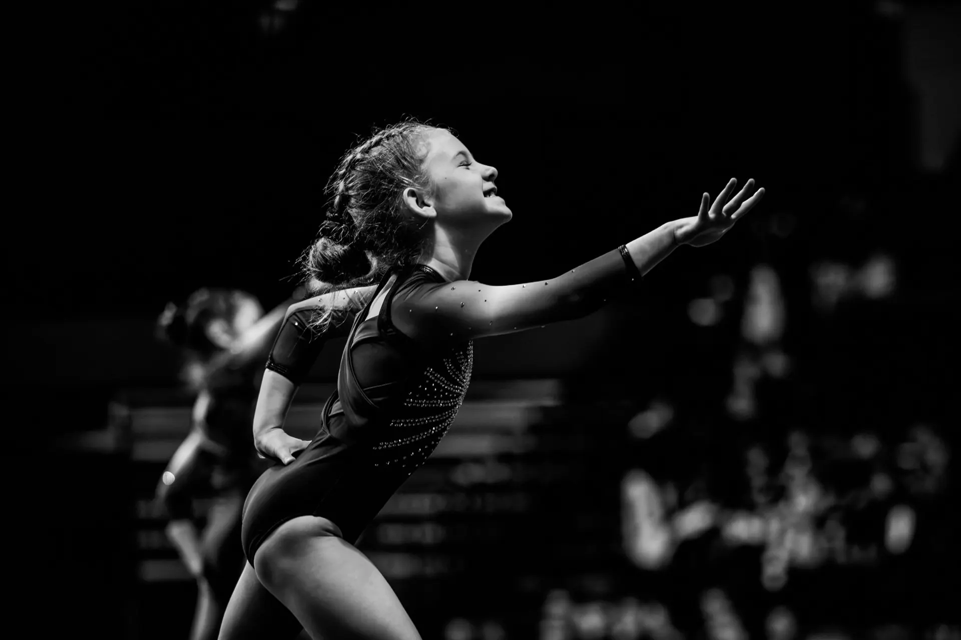 A performer reaching upward, in black and white, under moving haze beams